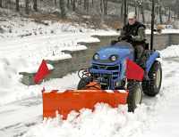 Traktor LS řady J vybavený čelní hydraulicky ovládanou sněhovou radlicí při úklidu sněhu